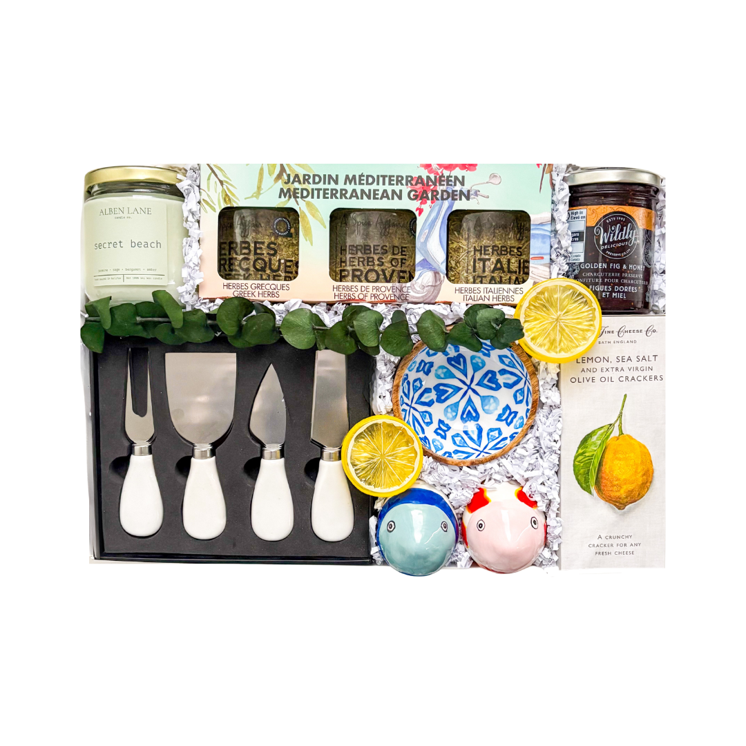 Signature gift box featuring Mediterranean-inspired gourmet treats and entertaining essentials including cheese knives, herb blends, olive oil crackers, olives, pistachios, brie cheese, dipping bowls, candle, and gourmet accompaniments.


