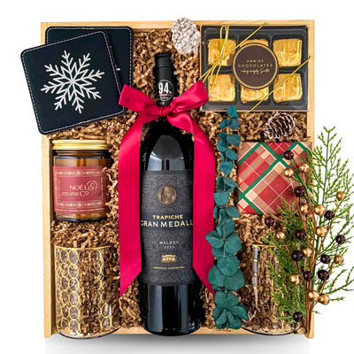 The Holiday Reserve luxury Christmas gift featuring red wine, two gold-accented glasses, gourmet chocolates, shortbread, festive candle, snowflake coasters and wooden keepsake tray.