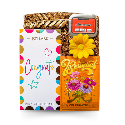 The Congrats Box with vibrant chocolate bar, word magnets, and a candle or seed pack styled as a bright, modern celebration gift.