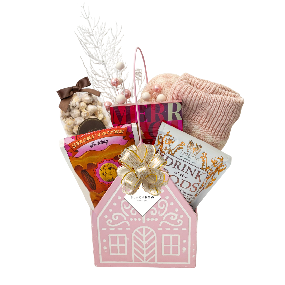 The Cozy Cottage gift basket featuring blush pink reading socks, roasted chestnut candle, gourmet chocolates, sweet treats and a pink cottage keepsake basket.