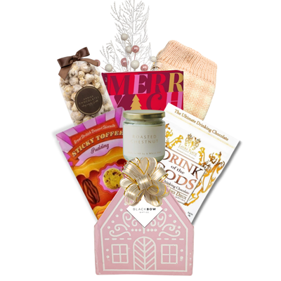 The Cozy Cottage gift basket featuring blush pink reading socks, roasted chestnut candle, gourmet chocolates, sweet treats and a pink cottage keepsake basket.