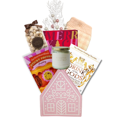 The Cozy Cottage gift basket featuring blush pink reading socks, roasted chestnut candle, gourmet chocolates, sweet treats and a pink cottage keepsake basket.