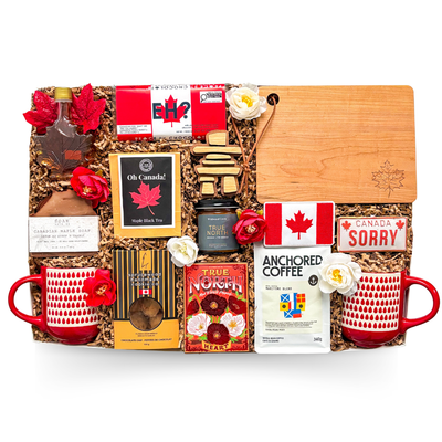 Luxury Canadian gift box featuring artisan coffee, pure Canadian maple syrup, pancake mix, maple black tea, artisan jam, maple soap, handcrafted cookies, Canadian mugs, engraved serving board, inukshuk décor, and premium Canadian-inspired keepsakes arranged in a layered presentation.