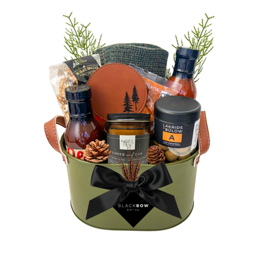 The Lodge Collection luxury gift basket featuring cozy knitwear, gourmet snacks, artisan sauces, a scented candle and leather accessories in an olive green metal keepsake caddy.
