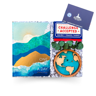Travel-themed gift box featuring a journal, travel challenge cards, keepsake ornament, and gourmet treats presented by Black Bow Gift Co.
