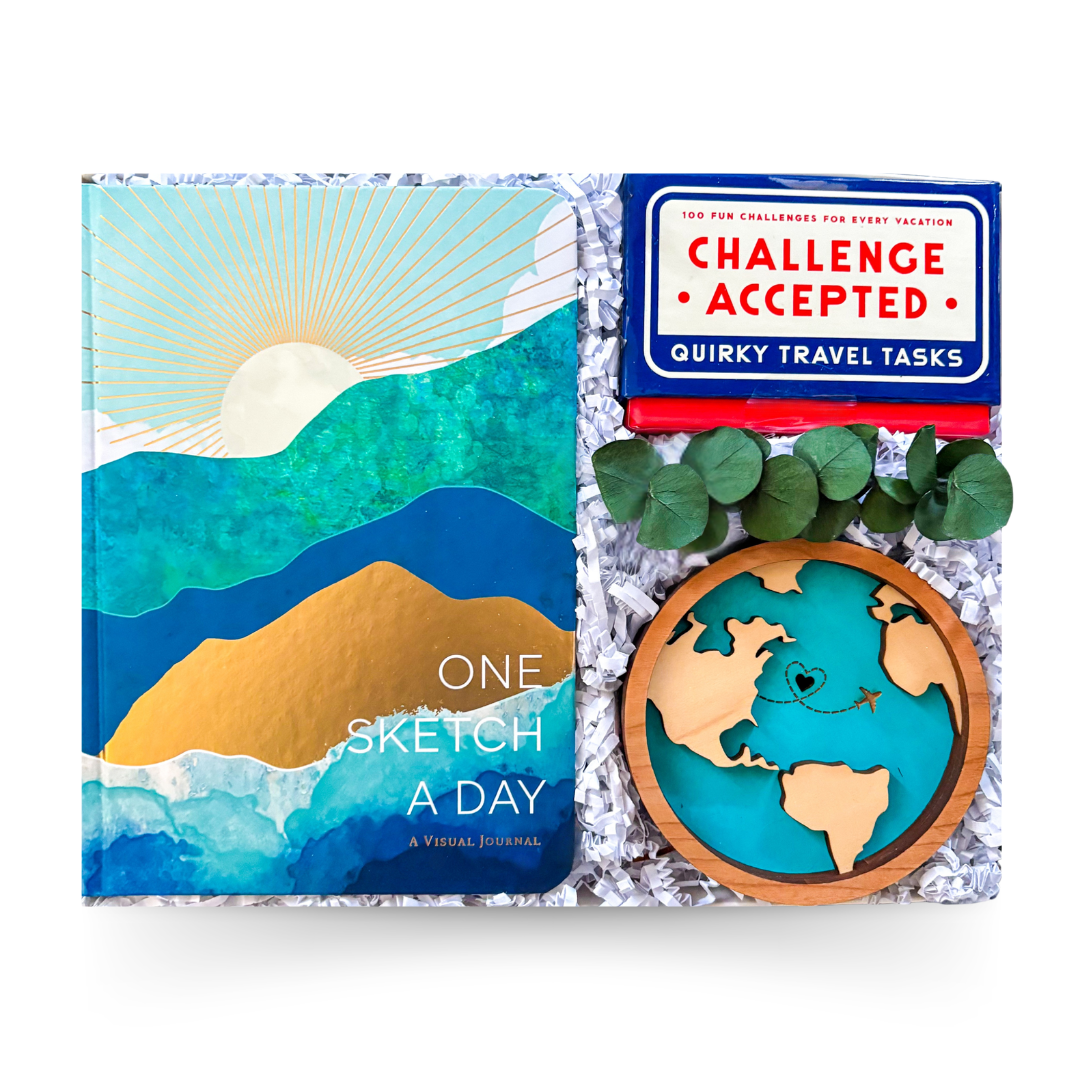 Travel-themed gift box featuring a journal, travel challenge cards, keepsake ornament, and gourmet treats presented by Black Bow Gift Co.