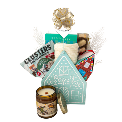 Winter Wonderland Christmas gift featuring cozy ivory fingerless gloves, candle, chocolates and festive treats in a light blue gingerbread house keepsake basket.
