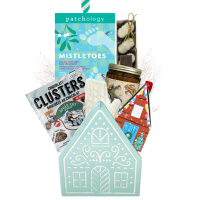 Winter Wonderland Christmas gift featuring cozy ivory fingerless gloves, candle, chocolates and festive treats in a light blue gingerbread house keepsake basket.