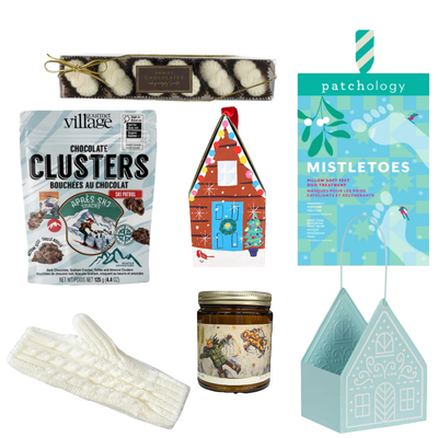 Winter Wonderland Christmas gift featuring cozy ivory fingerless gloves, candle, chocolates and festive treats in a light blue gingerbread house keepsake basket.