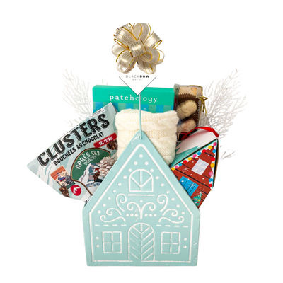 Winter Wonderland Christmas gift featuring cozy ivory fingerless gloves, candle, chocolates and festive treats in a light blue gingerbread house keepsake basket.