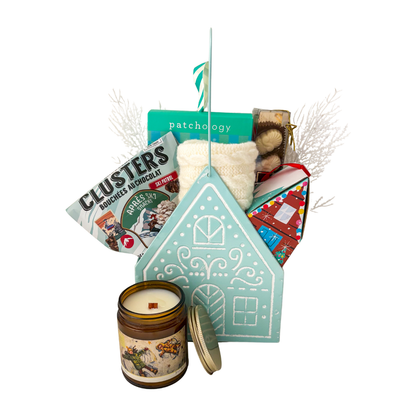 Winter Wonderland Christmas gift featuring cozy ivory fingerless gloves, candle, chocolates and festive treats in a light blue gingerbread house keepsake basket.