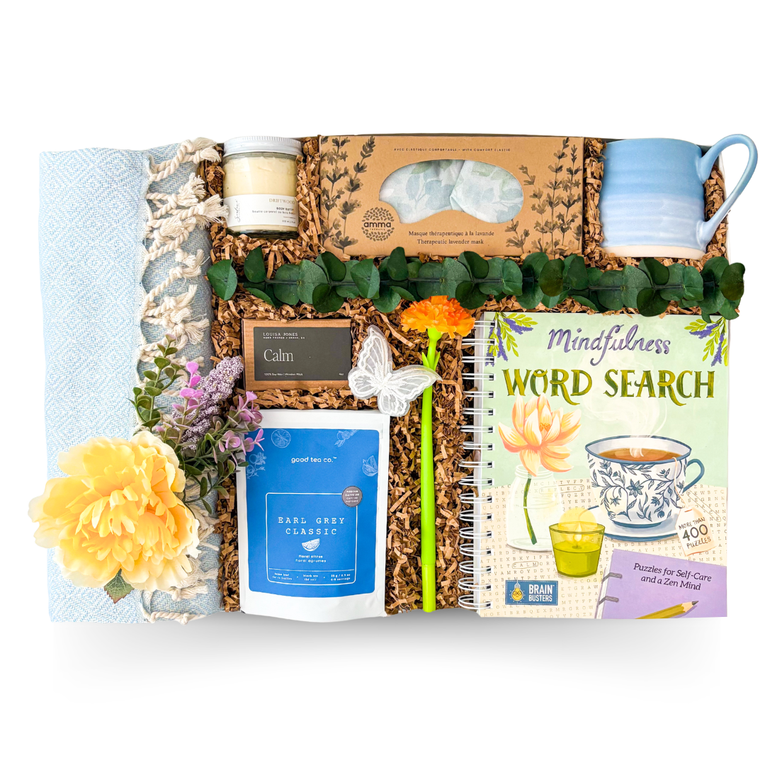 Luxury relaxation gift box featuring a cozy throw blanket, Earl Grey tea, calming candle, therapeutic eye pillow, keepsake mug, and mindfulness word search book for peaceful moments.

