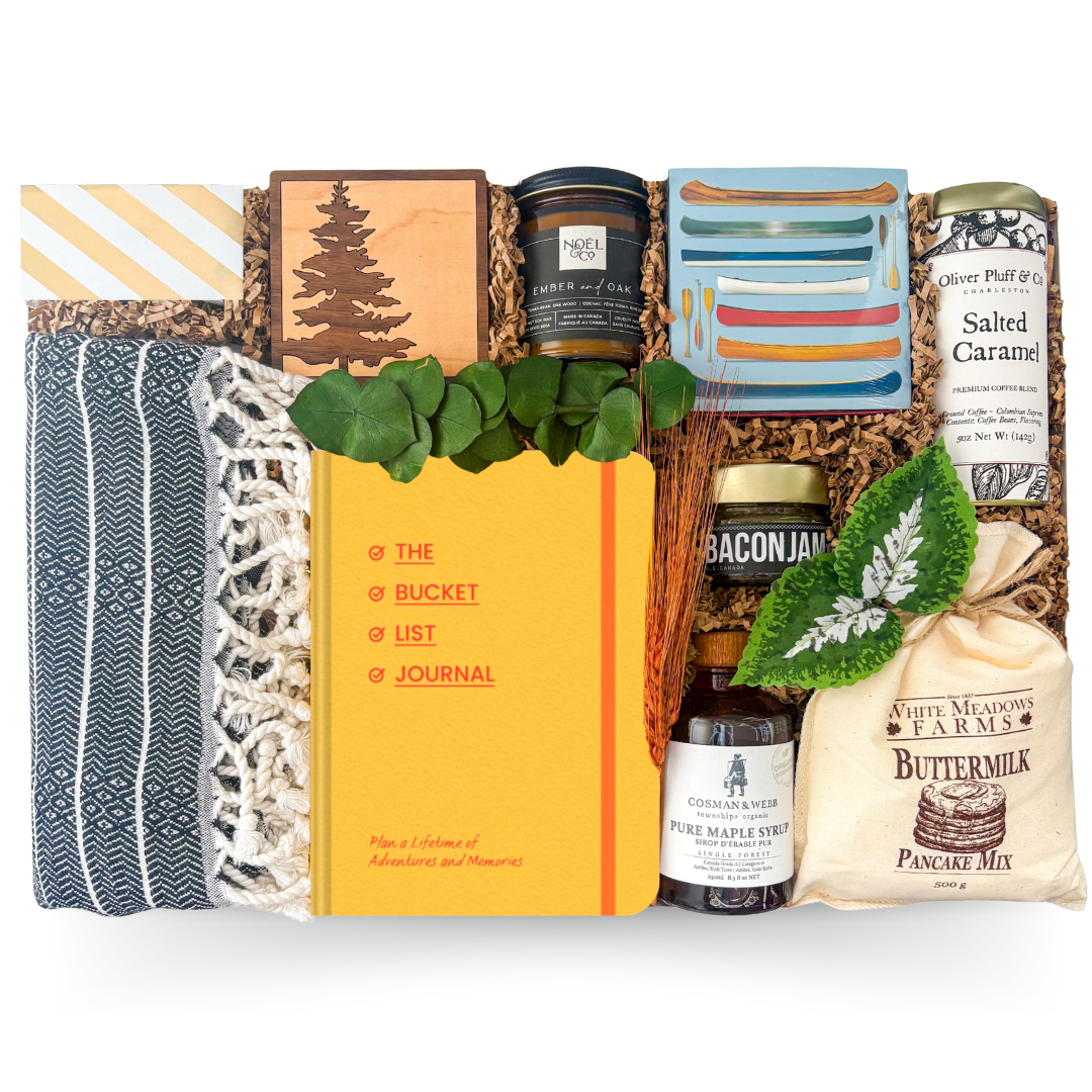 Gift basket with a variety of items including a journal, candles, and pancake mix on a white background.