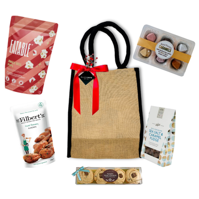 Gift bag with a red ribbon surrounded by various snacks on a white background