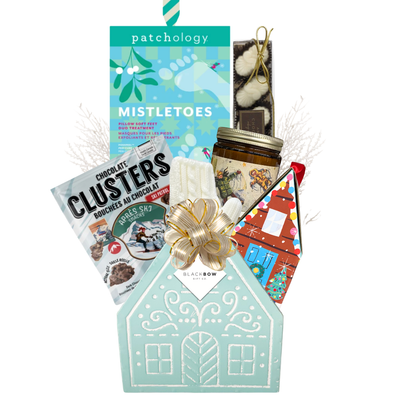 Winter Wonderland Christmas gift featuring cozy ivory fingerless gloves, candle, chocolates and festive treats in a light blue gingerbread house keepsake basket.