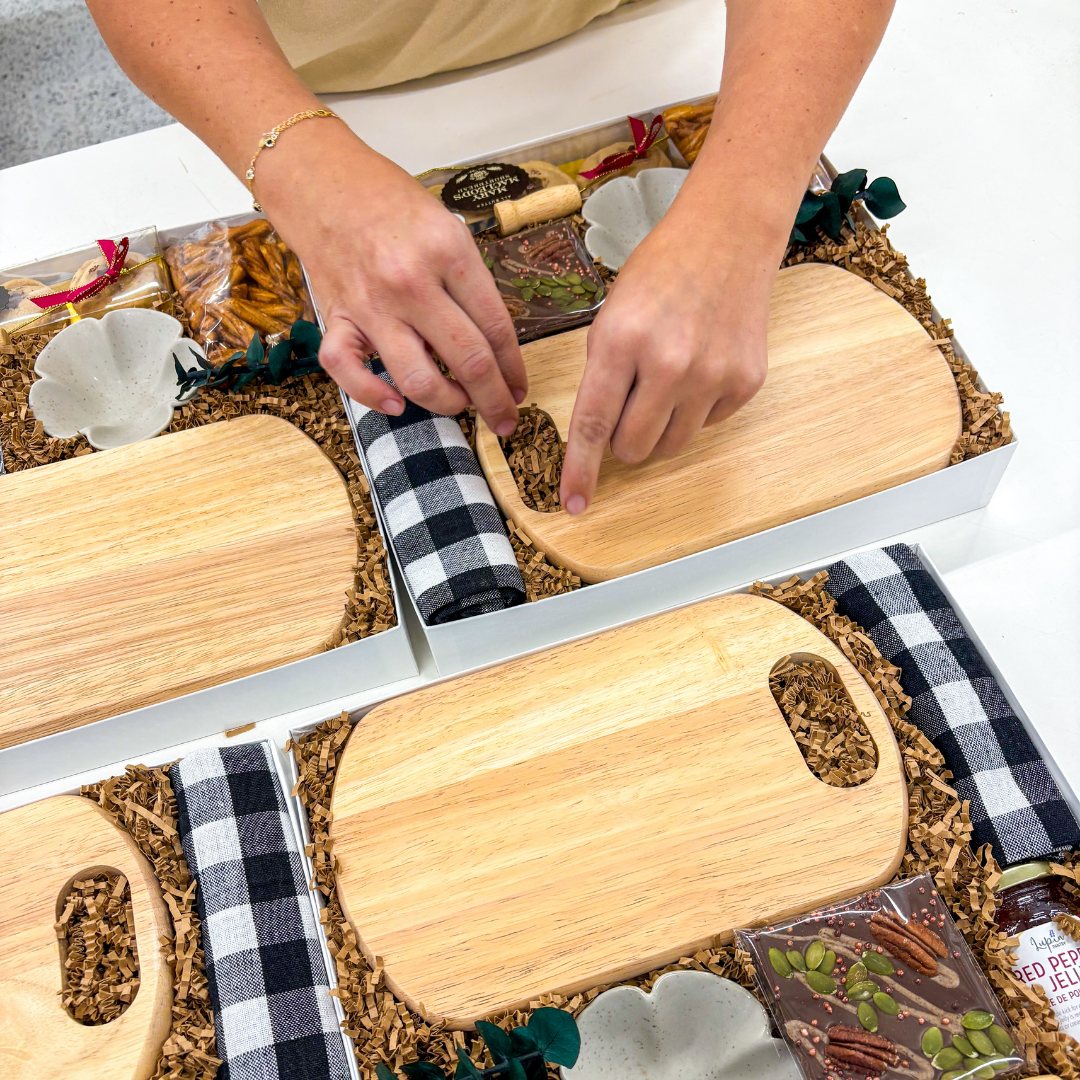 Hands arranging products and tying a plaid ribbon on wooden boards.