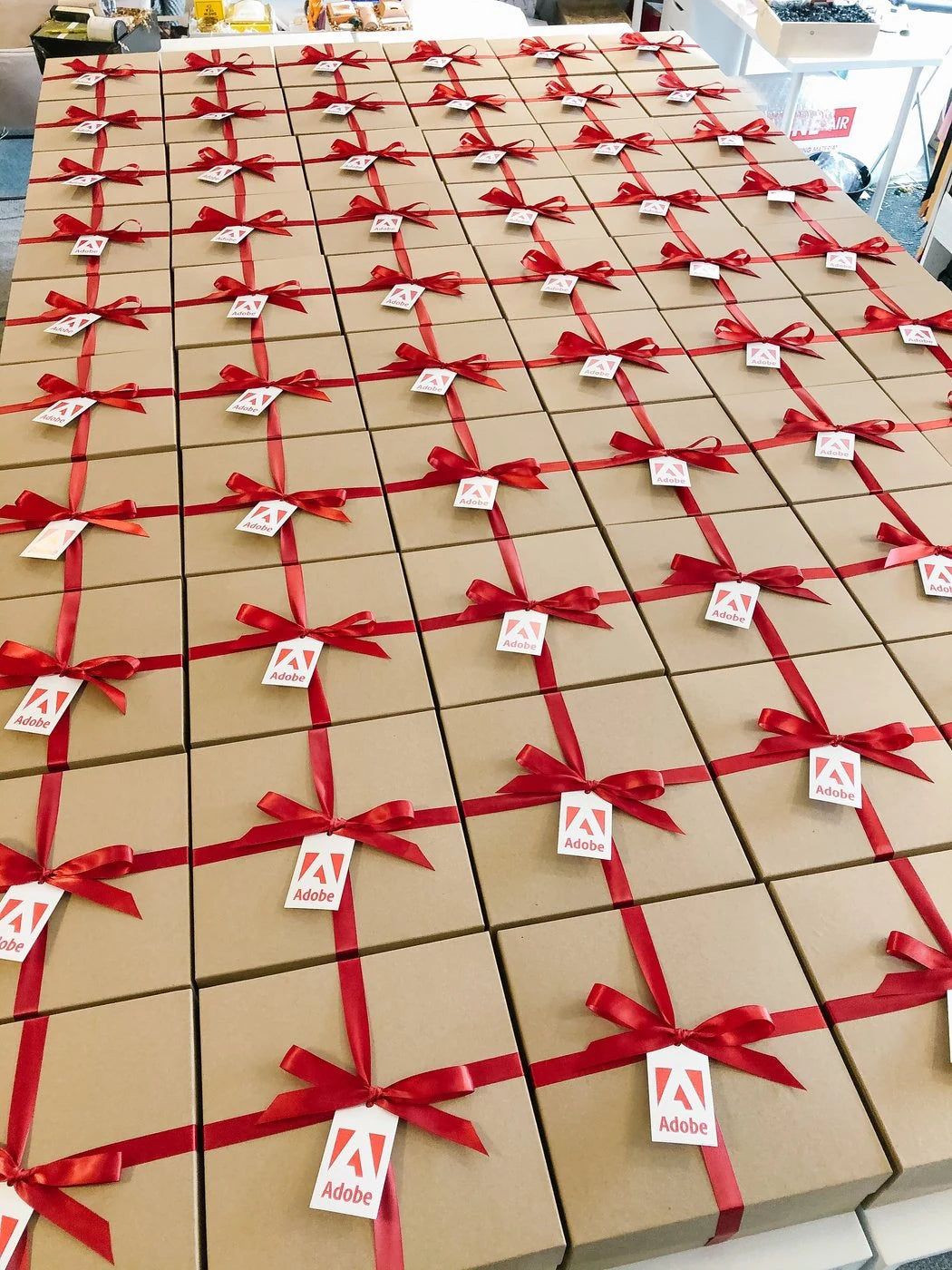 A long table of identical kraft boxes tied with red ribbon and Adobe tags.
