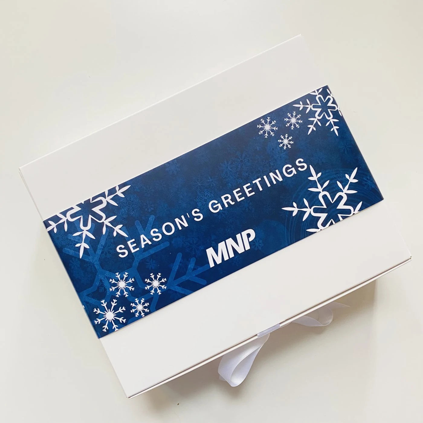 A white gift box wrapped in a custom MNP Season’s Greetings belly band.