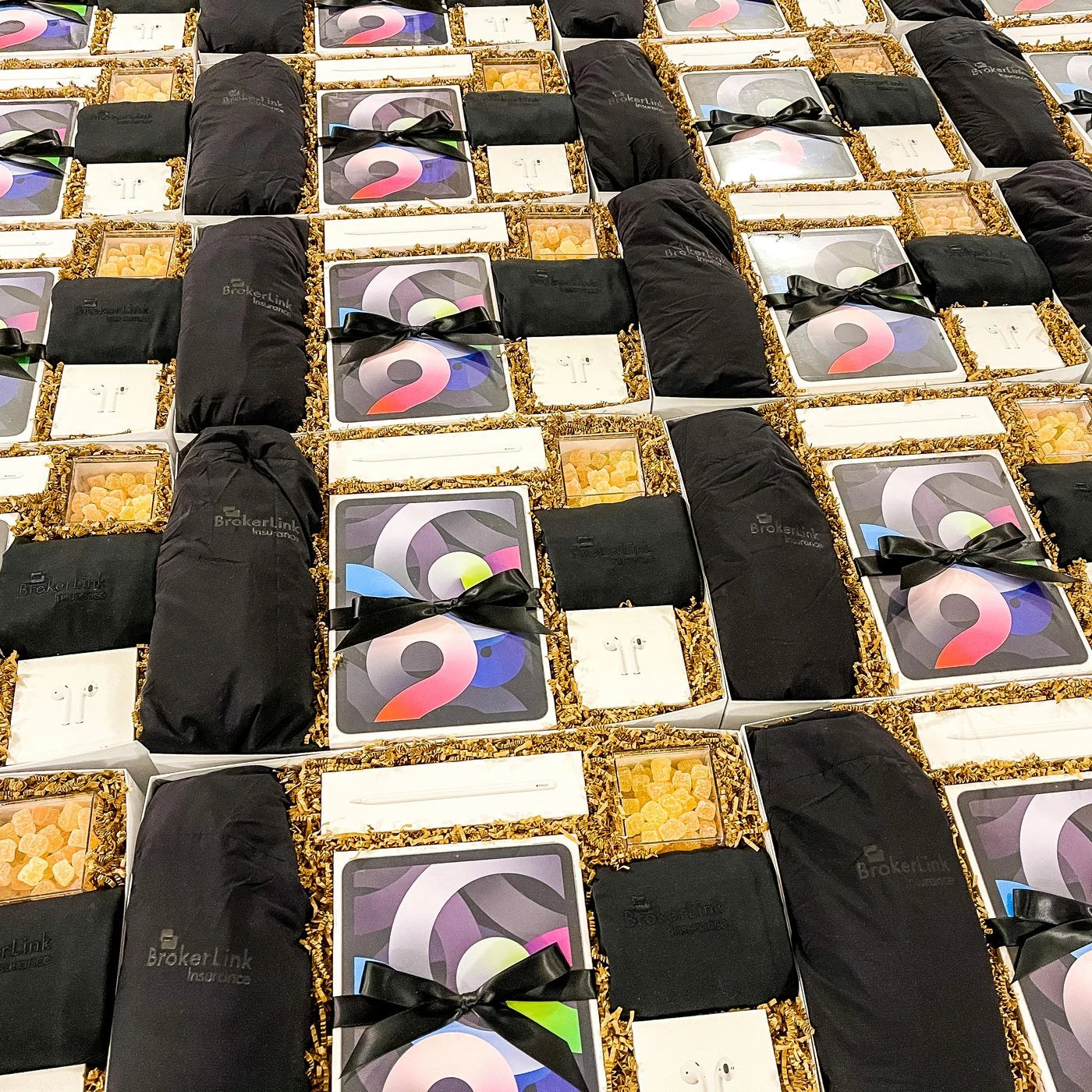 Rows of BrokerLink gift boxes with branded apparel, tablets and treats being packed.